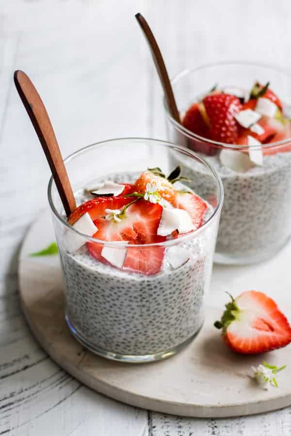 glass cups of coconut chia pudding with wooden spoons sticking out, topped with healthy breakfast toppings 
