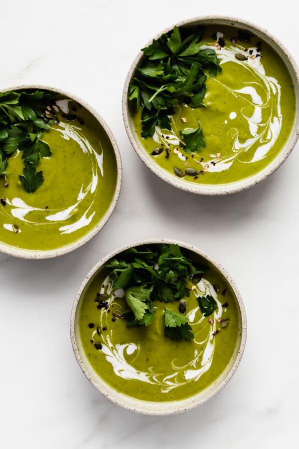 three bowls of broccoli soup topped with coconut milk and parsley