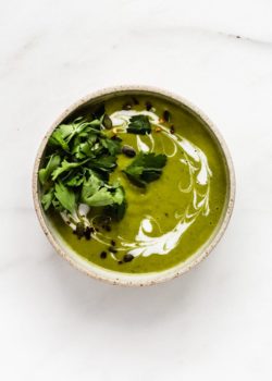 a bowl of broccoli soup topped with coconut milk and parsley