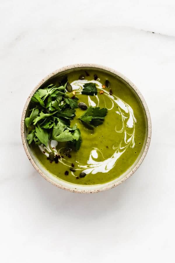 a bowl of broccoli soup topped with coconut milk and parsley