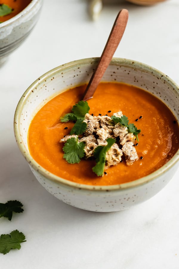 a bowl of orange soup topped with crumbled crackers and cilantro