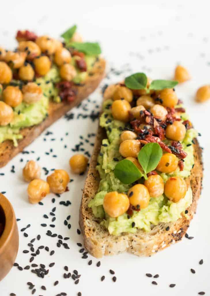 chickpeas on top of avocado toast, topped with black sesame seeds on a white plate