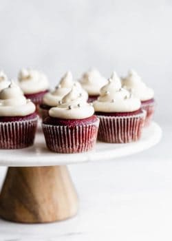 vegan red velvet cupcakes with cream cheese frosting and silver sprinkles on a marble and wood cakestand