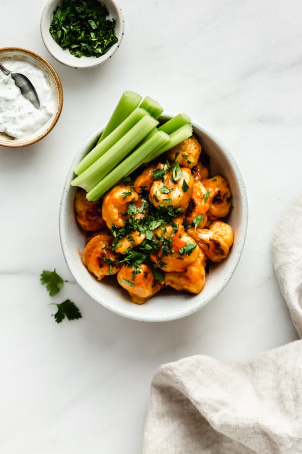 buffalo cauliflower wings in a bowl with a side of ranch sauce and chopped parsley