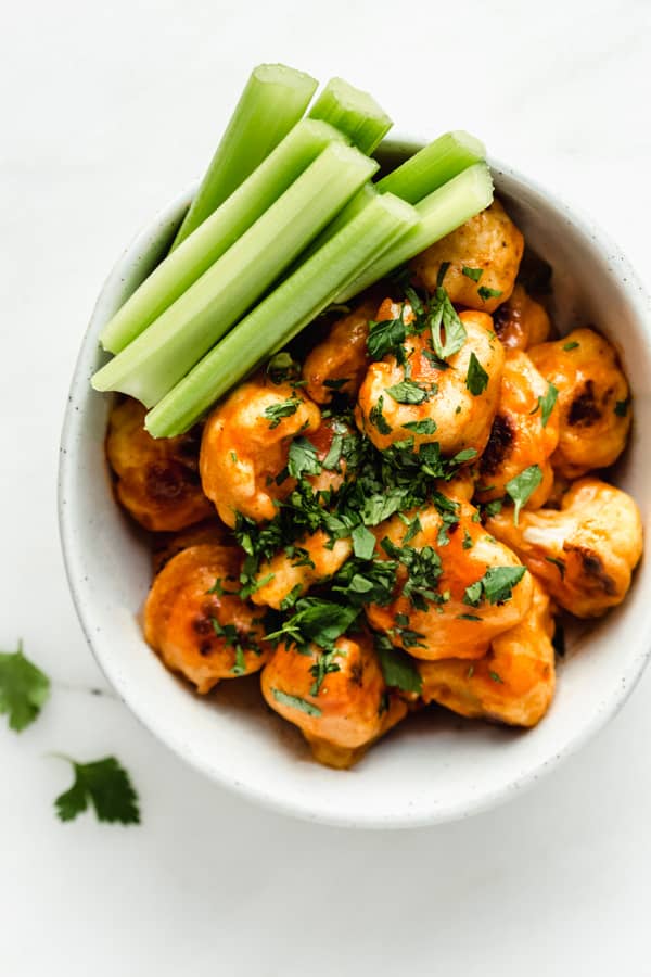 a bowl of buffalo cauliflower topped with parsly and a side of cut up celery sticks