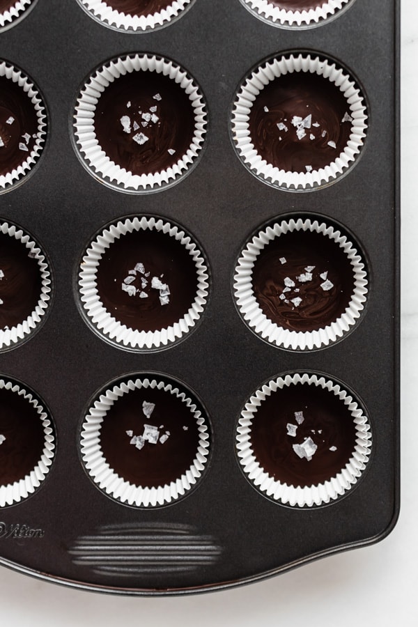 dark chocolate almond butter cups topped with flaked sea salt in a muffin pan