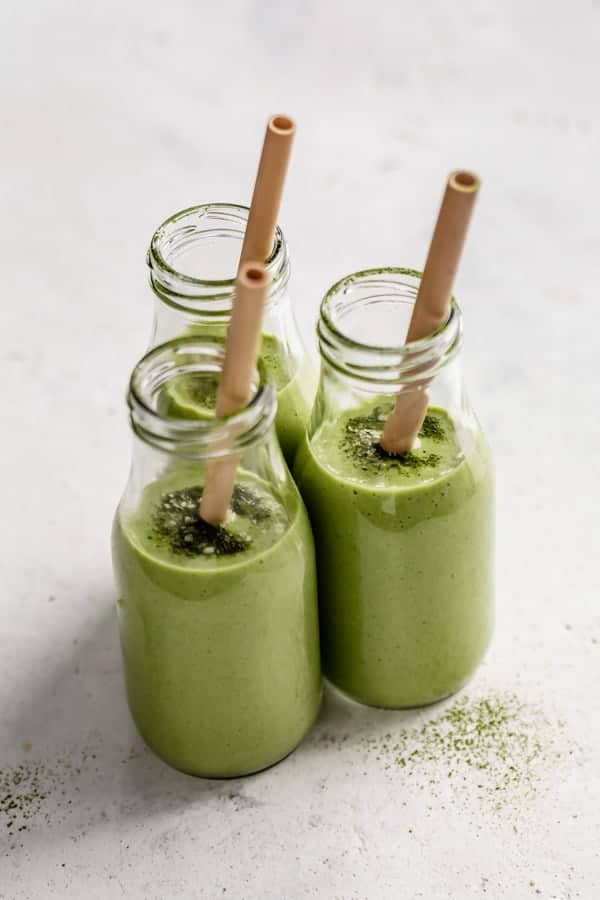 three jars of matcha green tea smoothies topped with matcha powder and straws in them