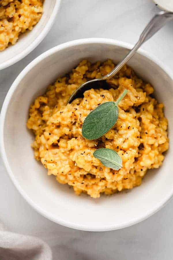 date night roasted butternut squash risotto topped with sage and black pepper in a white bowl with a silver spoon