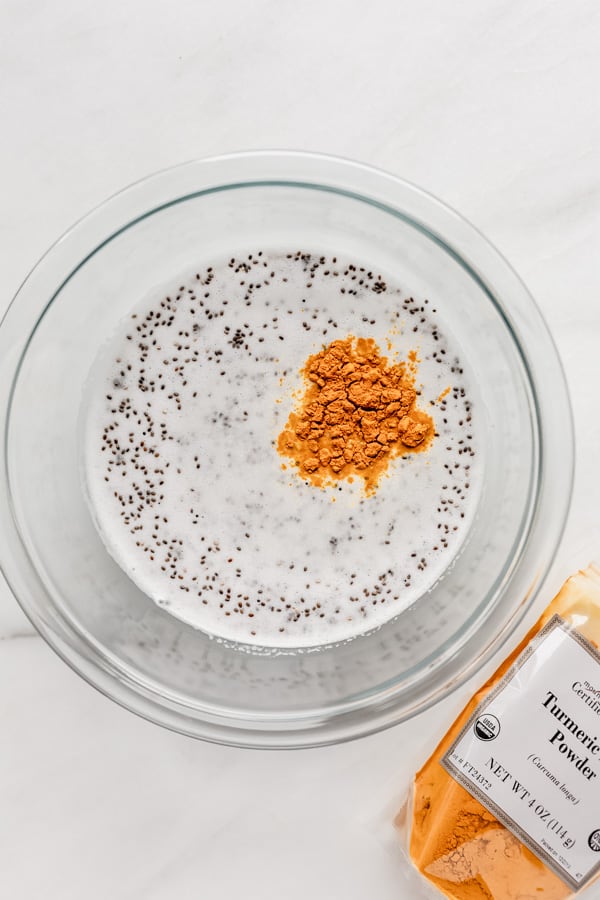 A clear mixing bowl with coconut milk, chia seeds and turmeric in it