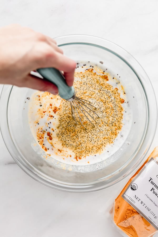 a hand whisking a bowl of chia seeds, coconut milk and turmeric