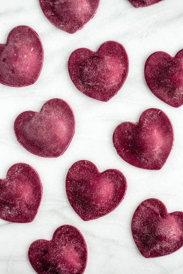 pink heart-shaped stuffed ravioli on a white marble pastry board