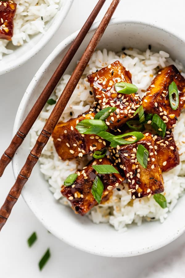 rice in a bowl with orange tofu green onions and sesame seeds