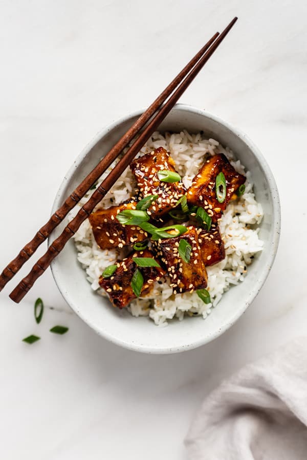 top down of a bowl of orange tofu with chopsticks on the side