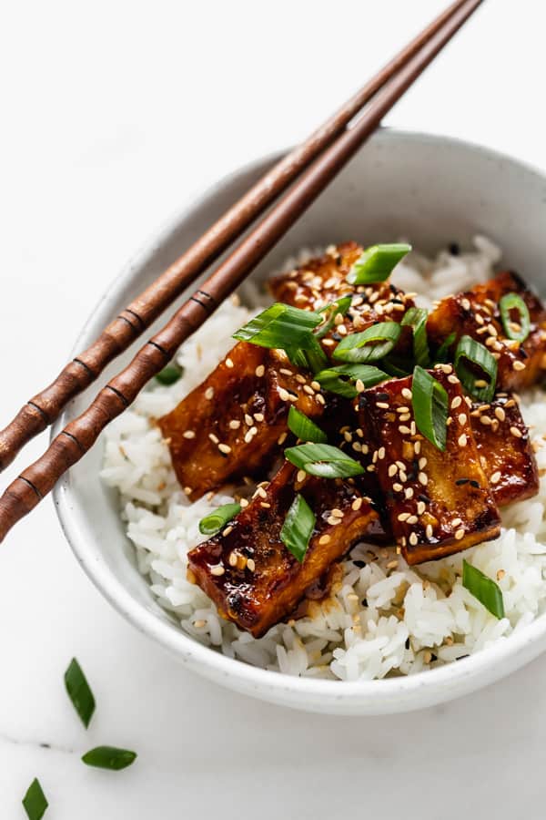 orange tofu in a bowl topped with green onions