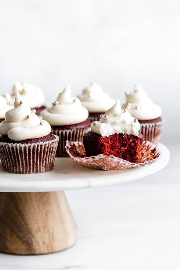 vegan red velvet cupcakes with a bite taken out of one cupcake on a marble and wood cake stand