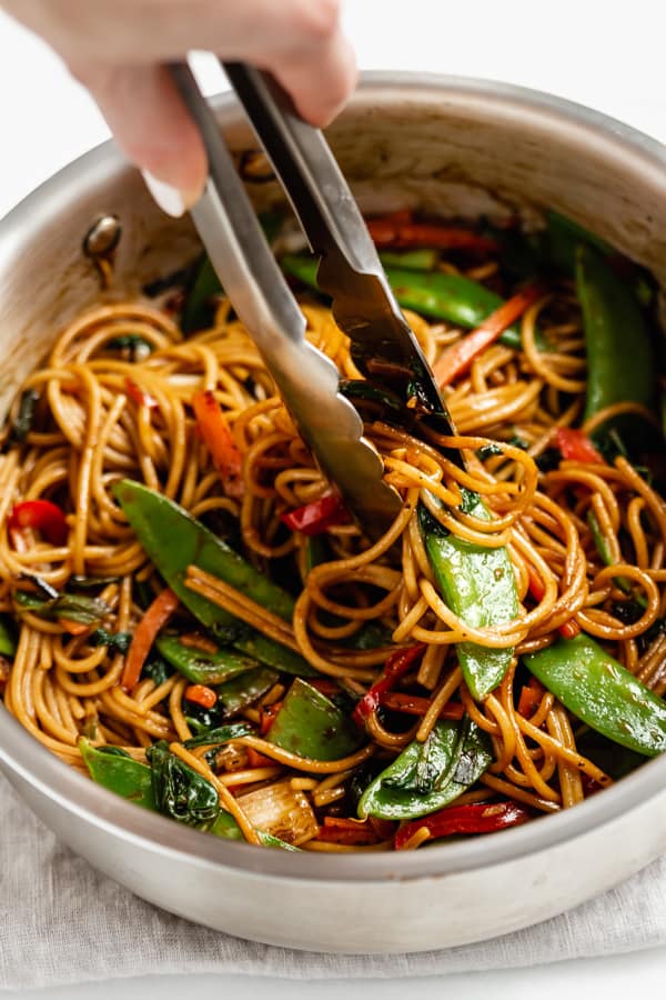 tongs scooping up vegetable lo mein from a pan