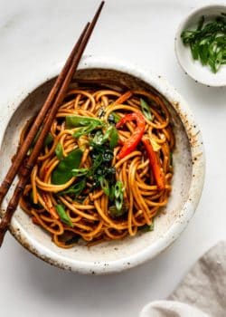 vegetable lo mein in a ceramic bowl with a side of sliced green onions