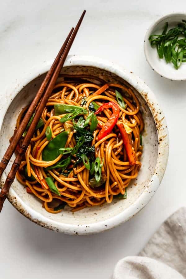 vegetable lo mein in a ceramic bowl with a side of sliced green onions