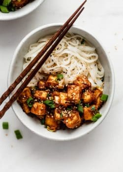 a bowl of noodles topped with peanut butte tofu, sesame seeds and green onions