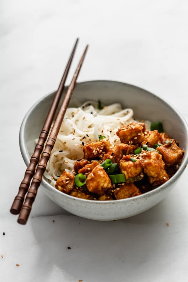 peanut butter tofu and noodles in a bowl with chopsticks on top