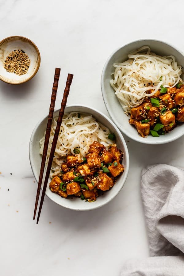two bowls of peanut butter tofu with a side of sesame seeds