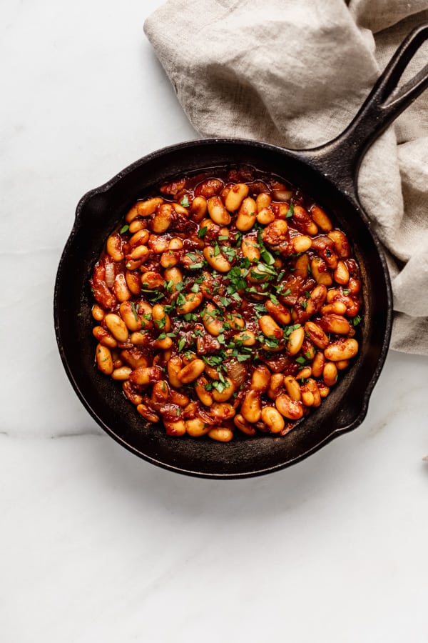 maple baked beans in a cast iron skillet with a beige napkin on the side