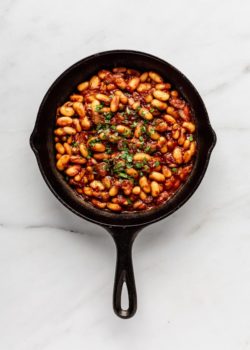 a cast iron skillet of maple baked beans on a marble counter