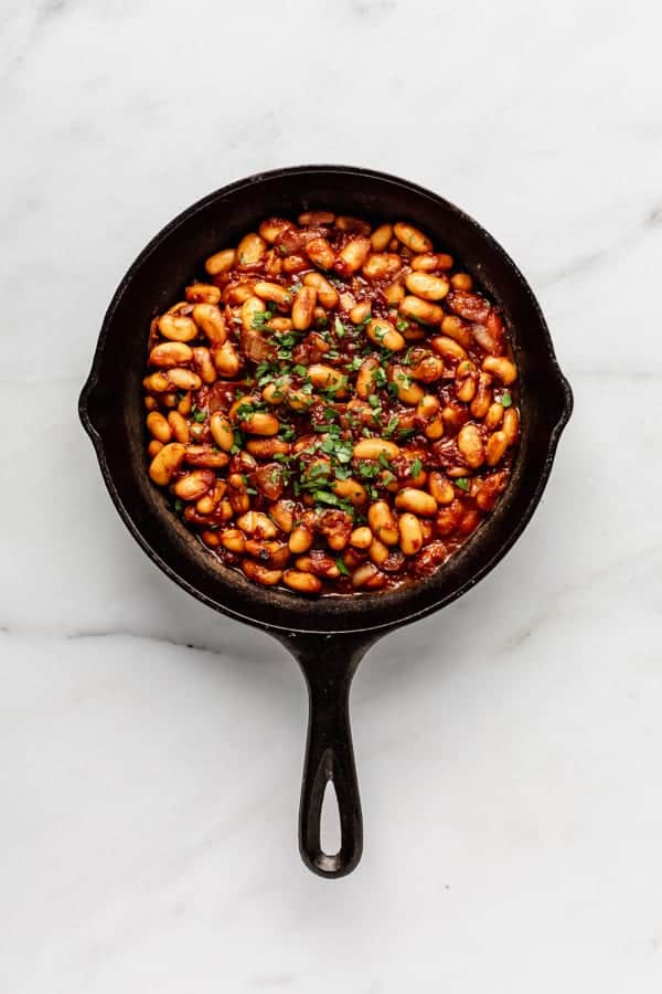 a cast iron skillet of maple baked beans on a marble counter