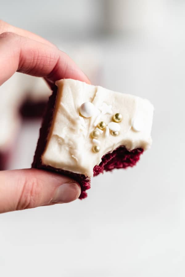 A hand holding a red velvet brownie with a bite taken out of it