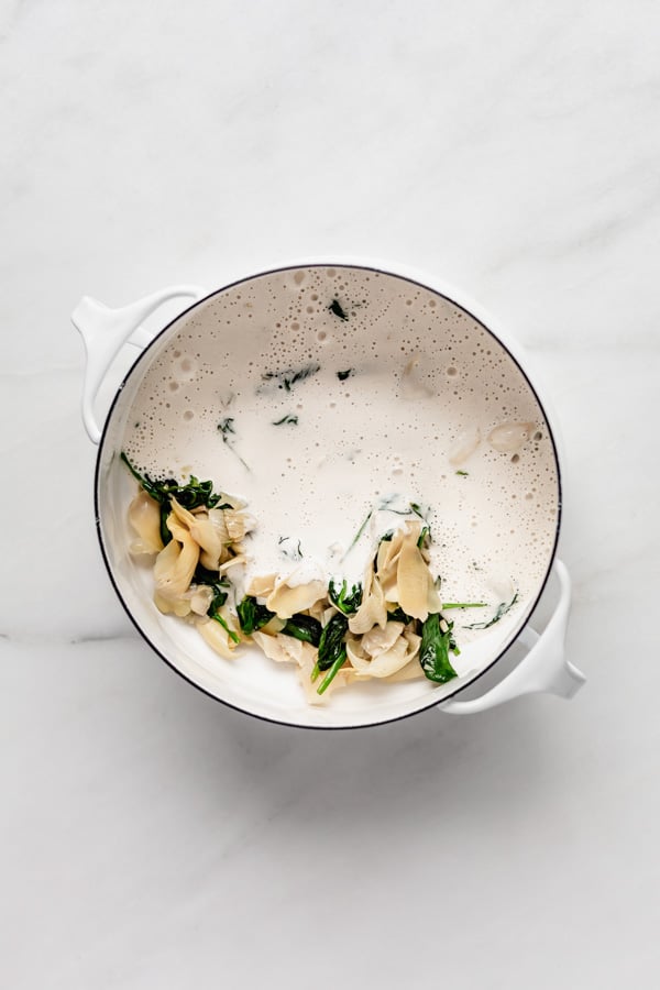 A white pot with spinach, artichoke hearts and vegan cream sauce in it