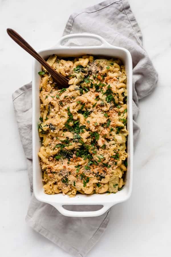 Vegan spinach and artichoke mac and cheese in a white baking dish with a serving spoon