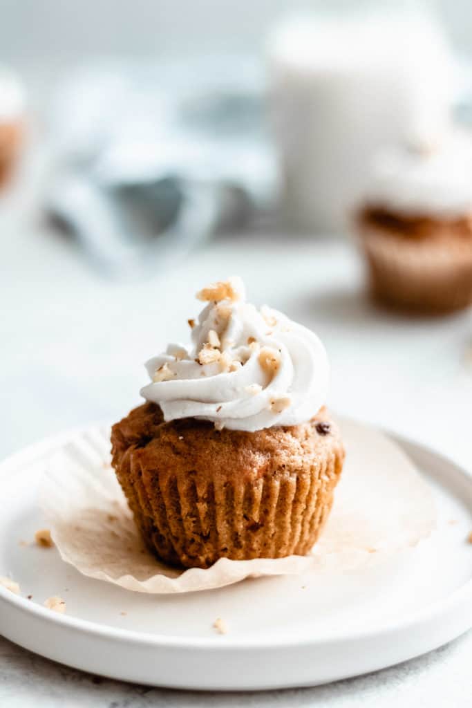 a carrot cupcake topped with coconut whipped cream and crushed walnuts