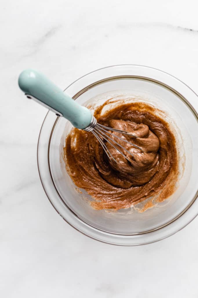 Almond butter in a clear mixing bowl with a whisk in it