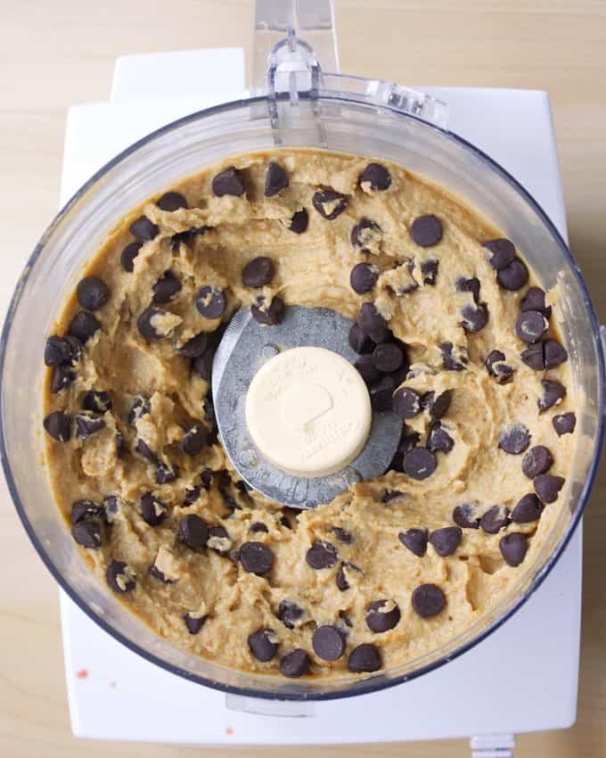 a white food processor filled with chocolate chip cookie dough made with a can of chickpeas