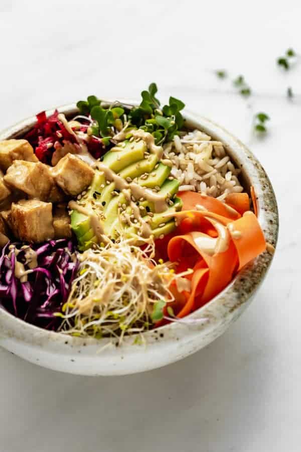 A bowl with tofu, vegetables and rice in it topped with dragon sauce