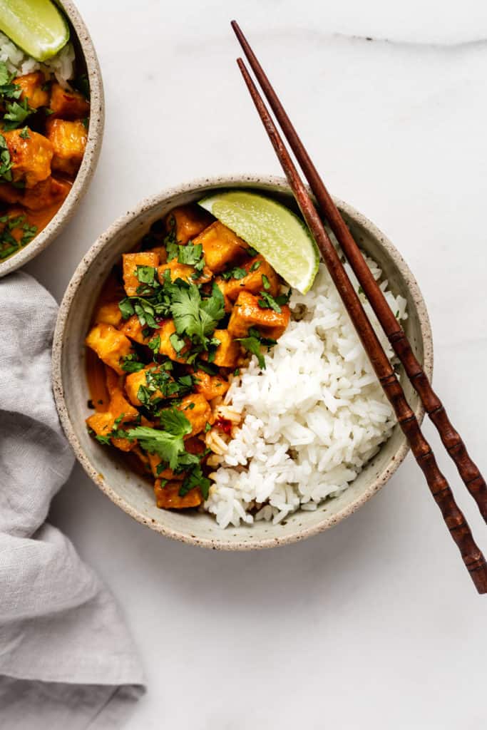 a bowl of coconut curry tofu with chopsticks on top and a napkin on the side