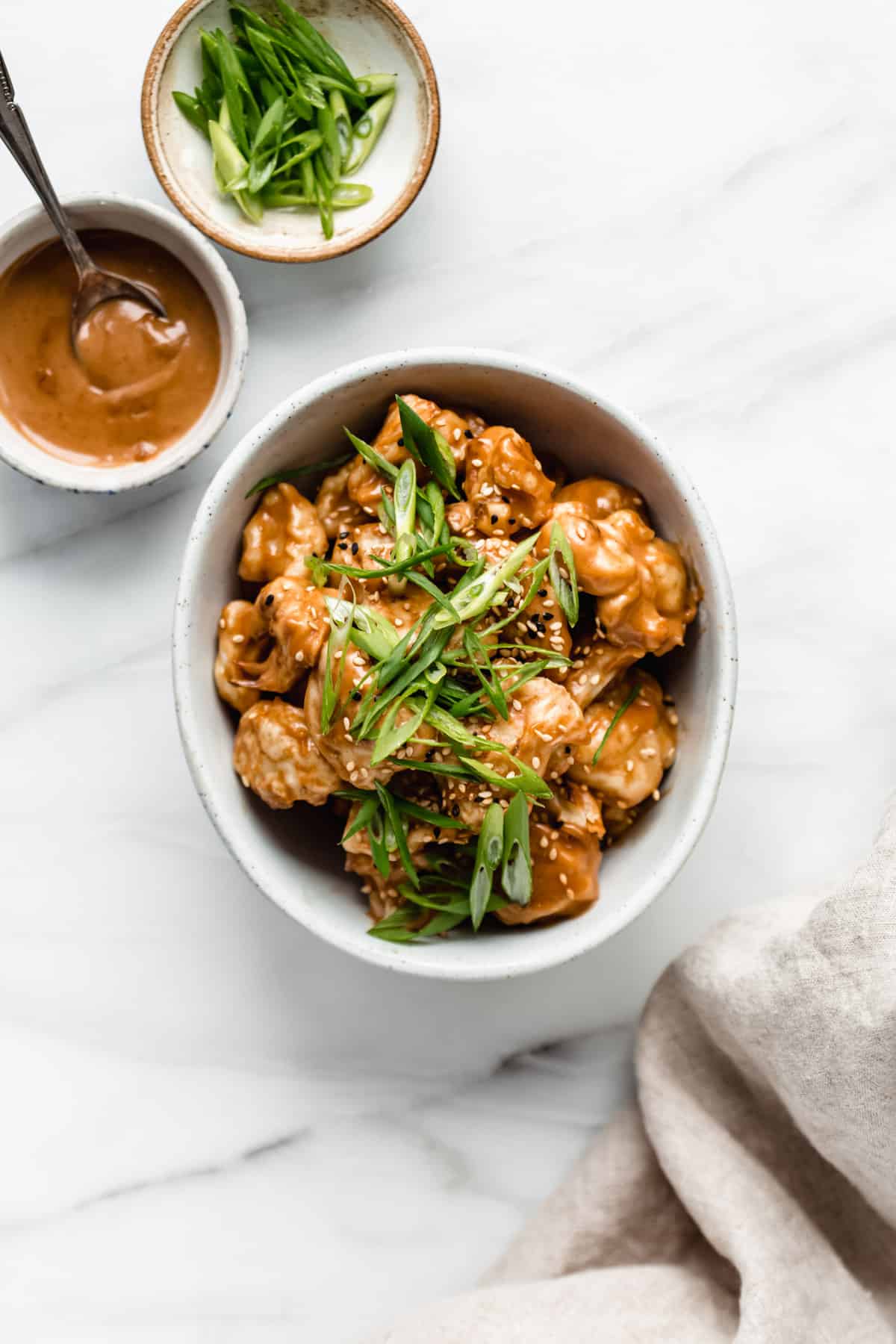 a bowl of Thai cauliflower wings with two small bowls on the side of peanut sauce and sliced green onions