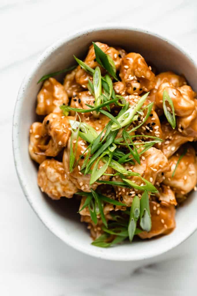 cauliflower in a bowl topped with peanut butter sauce and sliced green onions