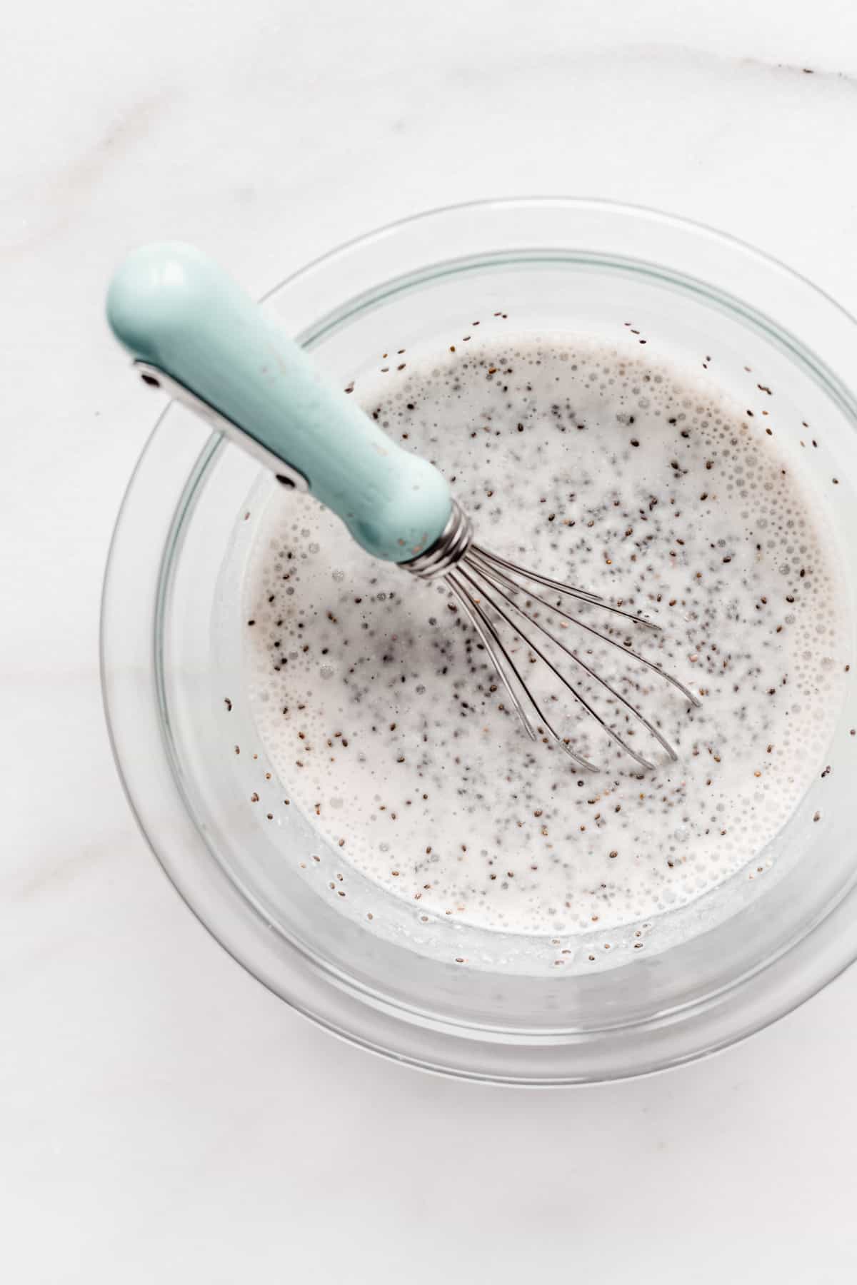 chia seeds and almond milk in a mixing bowl with a blue whisk