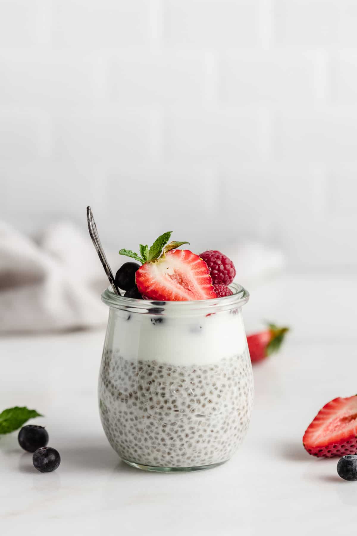 one small cup of vanilla chia pudding with a spoon and berries in it