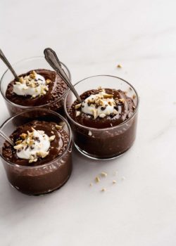 three cups of snickers chia pudding topped with yogurt, peanuts and cocoa nibs