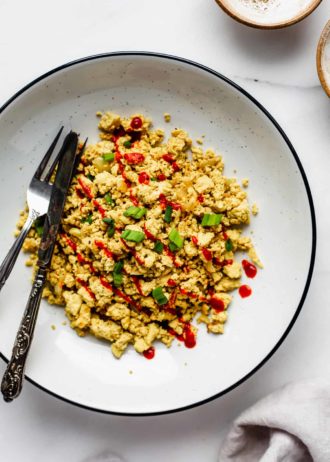 A bowl of scrambled tofu topped with chopped green onions and sriracha