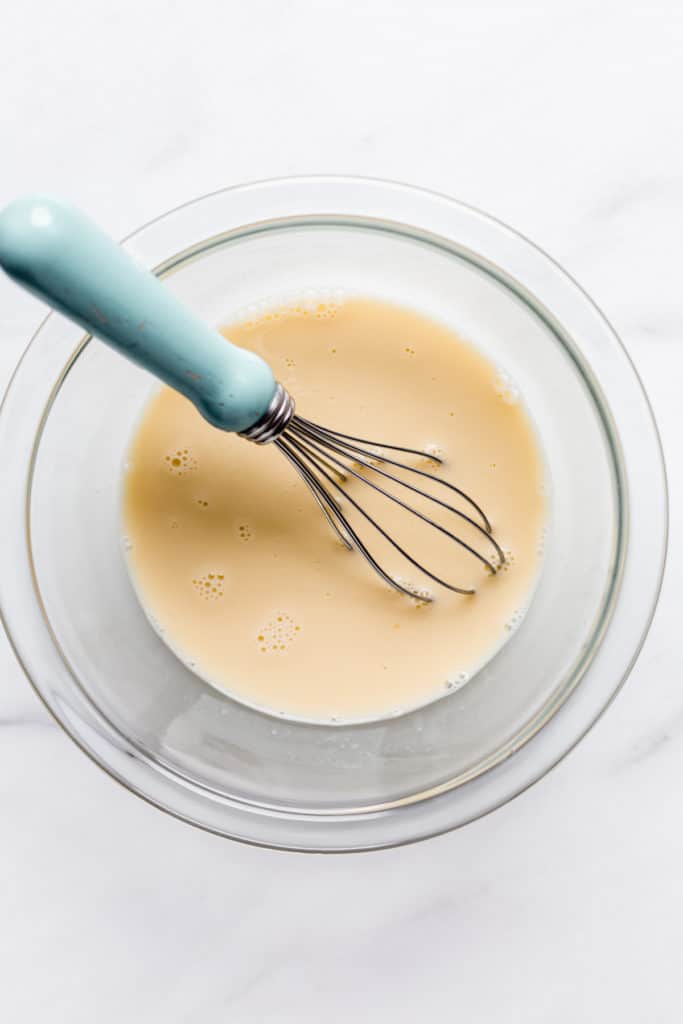 whisked eggs and coconut milk in a clear bowl with a small whisk in it