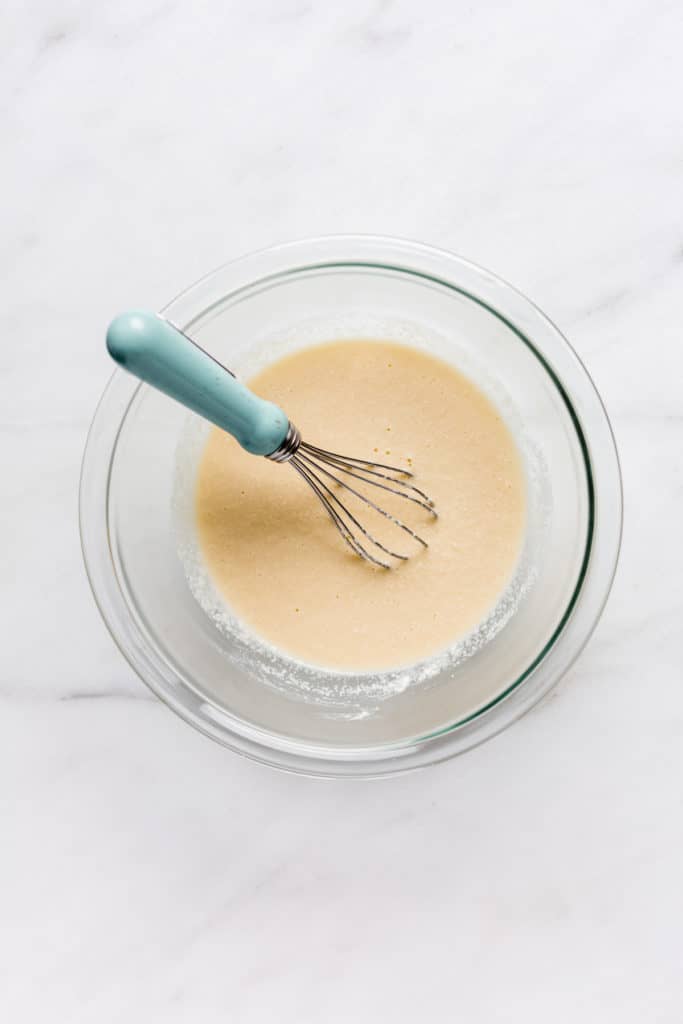 a clear mixing bowl with coconut flour pancake batter and a whisk in it