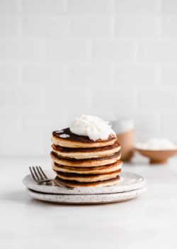 a stack of coconut flour pancakes on a white speckled plate with a fork on the side