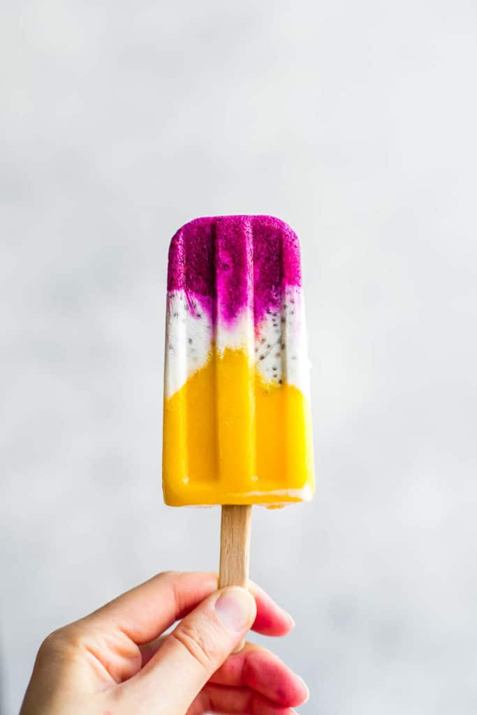 A hand holding a tropical coconut chia popsicle
