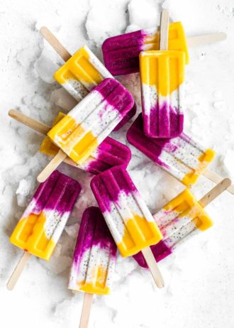 popsicles with layers of mango, coconut and dragonfruit on a board with ice