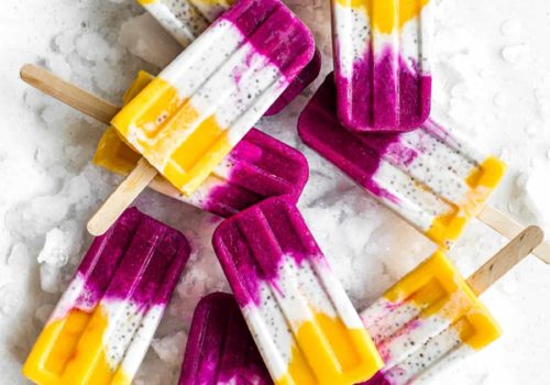 popsicles with layers of mango, coconut and dragonfruit on a board with ice