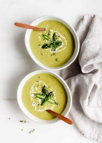 two bowls of vegan asparagus soup with wooden spoons in them and a napkin on the side