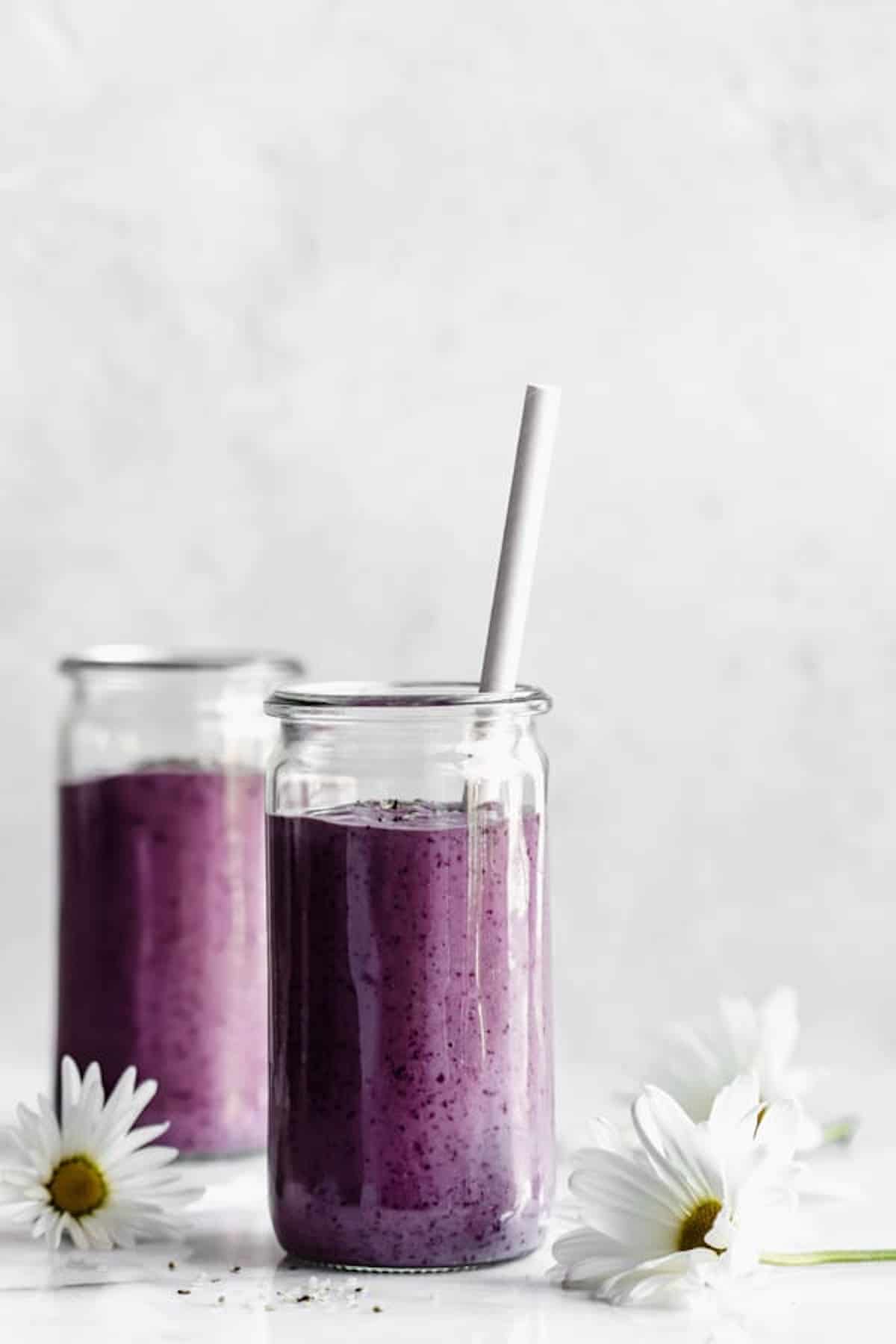 Two jars with purple smoothies in them with white flowers around them